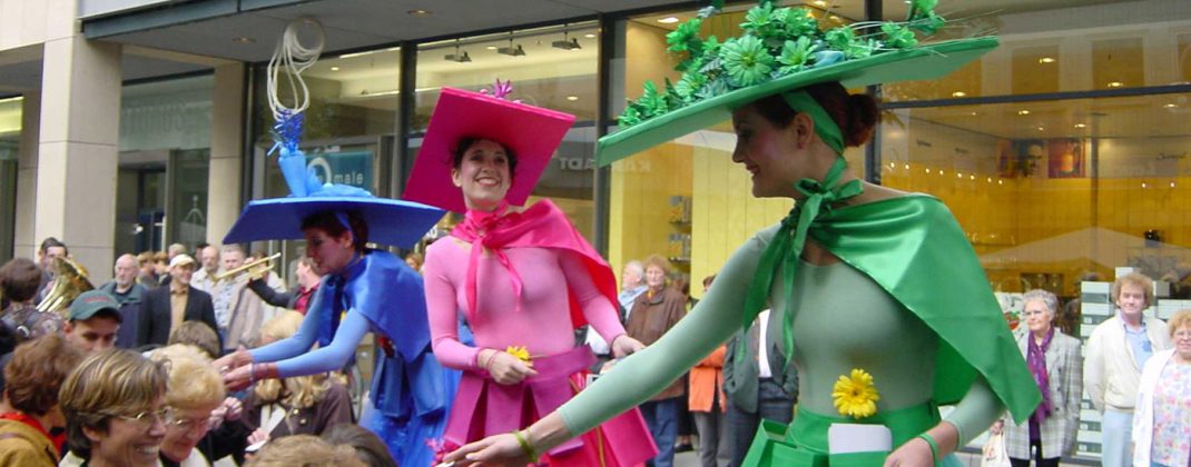 Drei Stelzenläuferinnen von der Künstlergruppe Corpus Titanium bei einer Eröffnungsveranstaltung in Kostümen des Veranstalters.