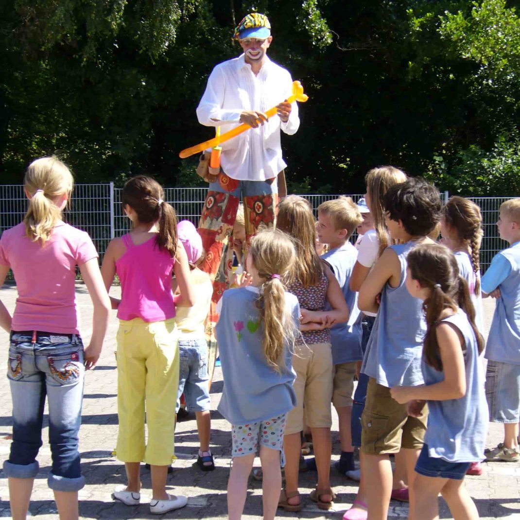 Ein Stelzen-Clown mit Ballonmodellage knotet Ballons für eine Gruppe Kinder-